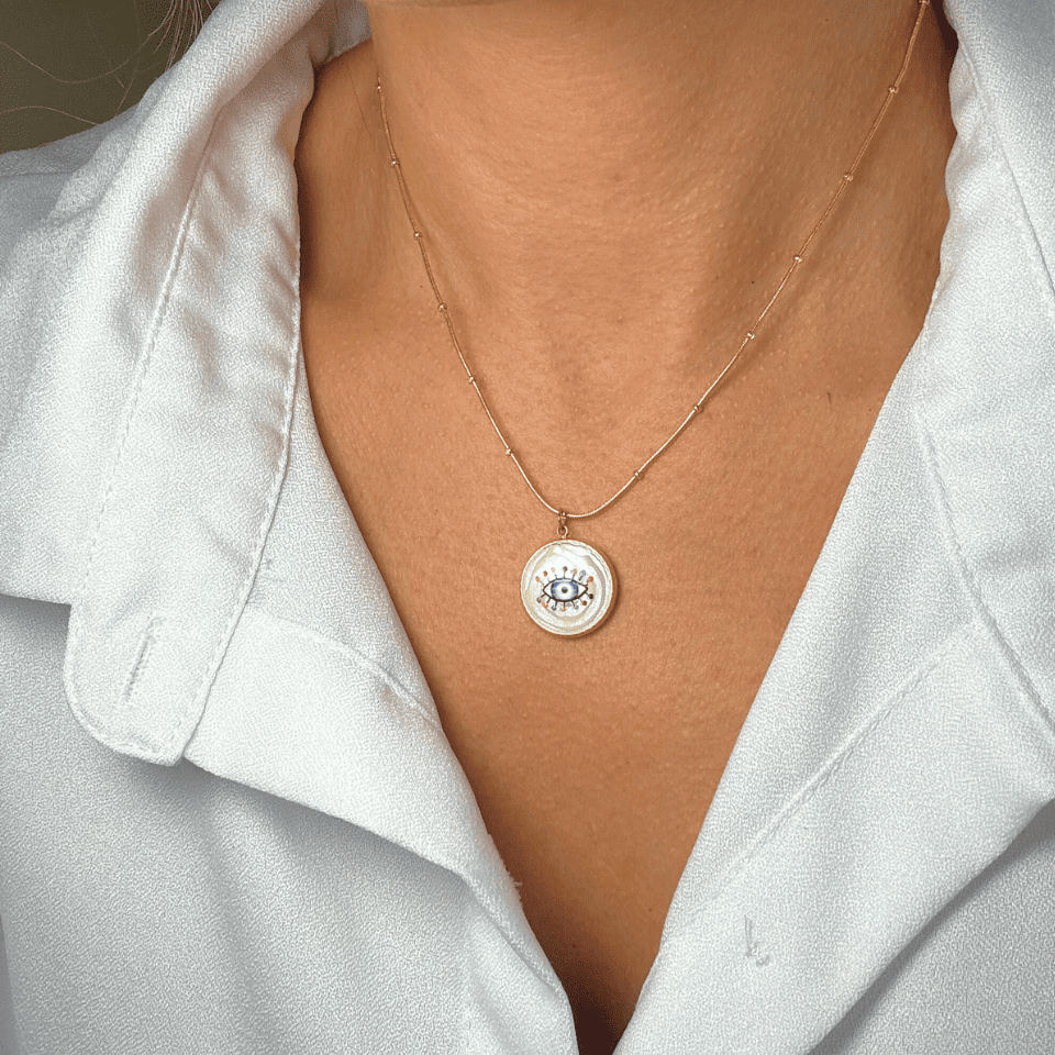 Necklace with a circular pendant worn by a person in a white shirt.