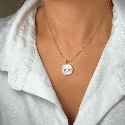 Necklace with a circular pendant worn by a person in a white shirt.