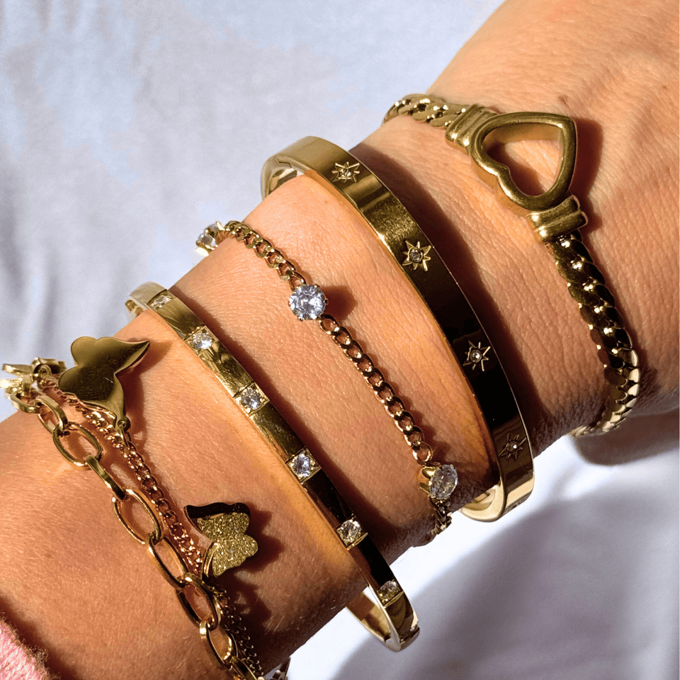 Close-up of a wrist wearing multiple gold bracelets with various designs on a light background.
