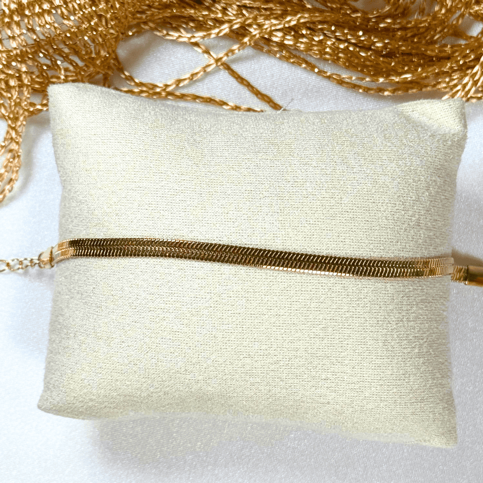 Gold bracelet on a white pillow with gold mesh in the background