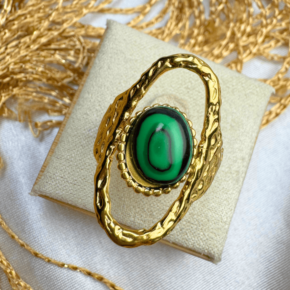 Gold brooch with green gemstone on a beige cushion, surrounded by gold chains.