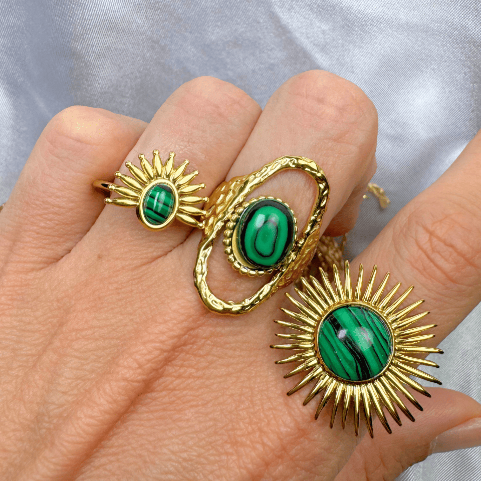 Gold earrings with green gemstones on a hand against a light background