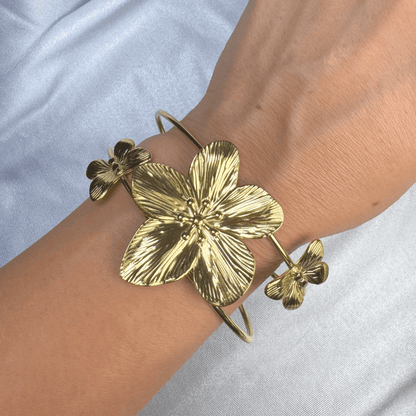 Gold floral bracelet on a wrist against a light blue background