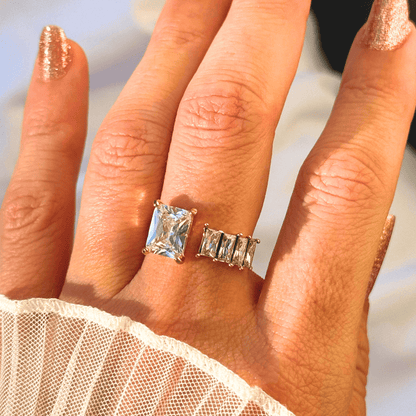 Hand wearing two gold rings with gemstones against a blurred background