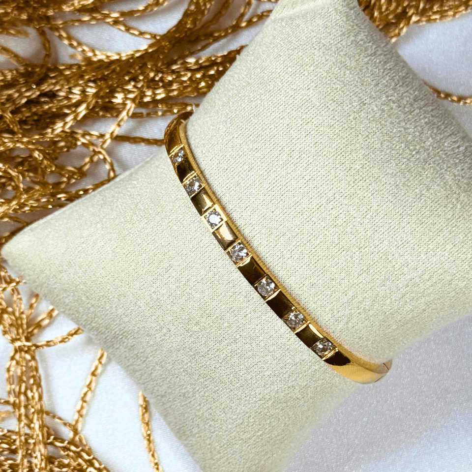 Gold bracelet with embedded stones on a beige cushion with gold chains in the background
