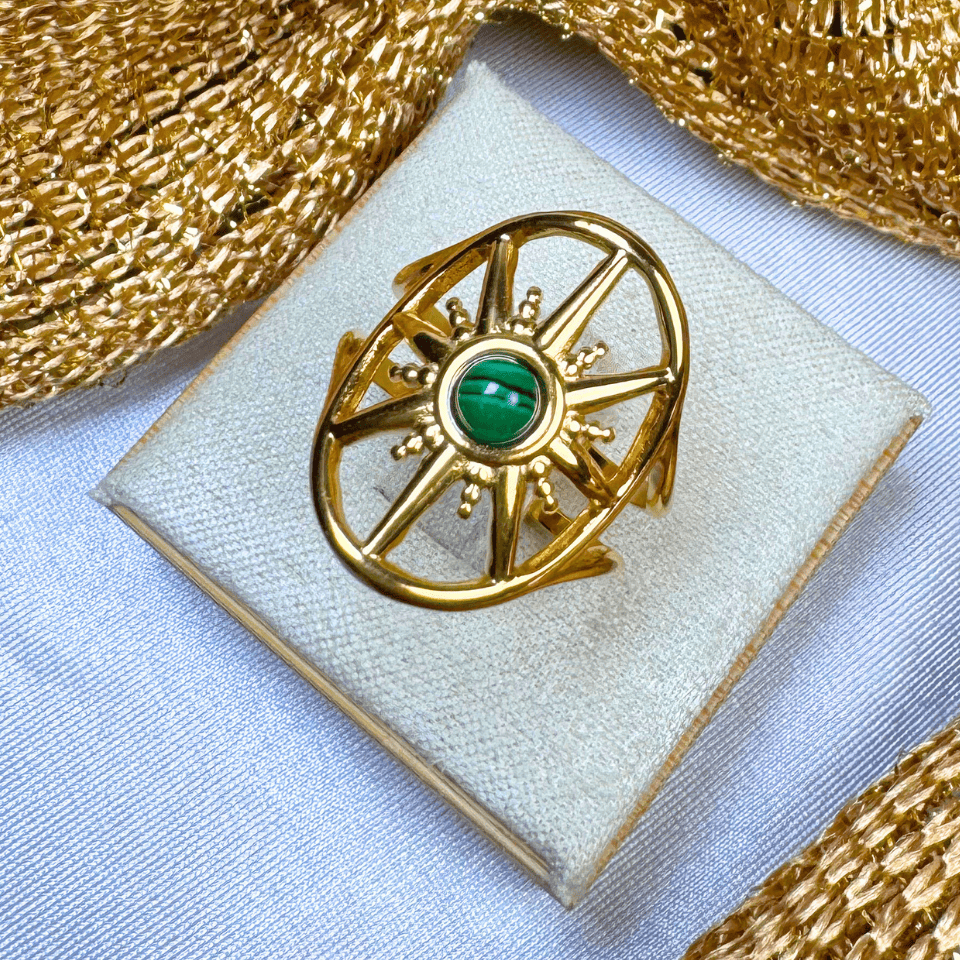 Gold ring with a green gemstone on a white cushion, surrounded by gold fabric.