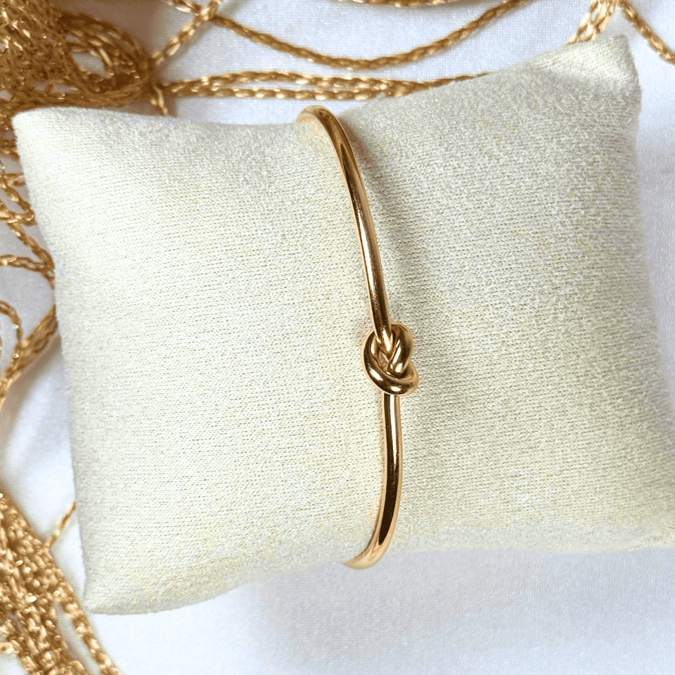 Gold bracelet with a knot design on a white pillow