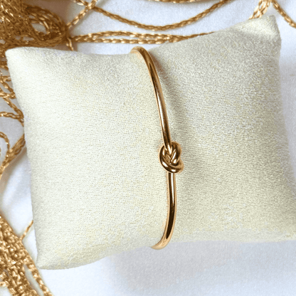 Gold bracelet with a knot design on a white pillow