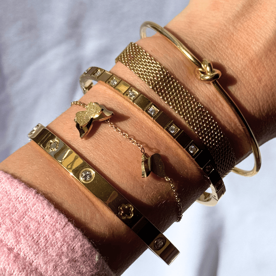 Close-up of a wrist wearing multiple gold bracelets with various designs.