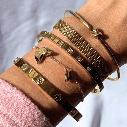 Close-up of a wrist wearing multiple gold bracelets with various designs.