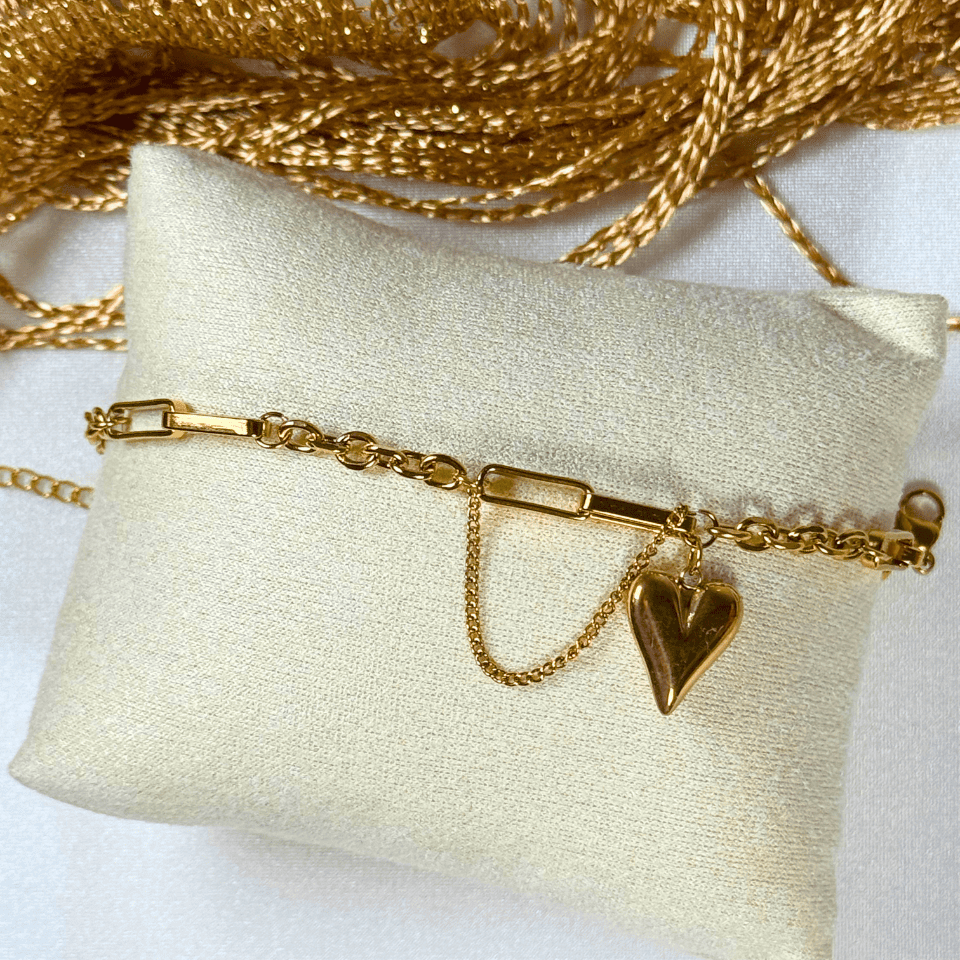 Gold bracelet with a heart charm on a white pillow