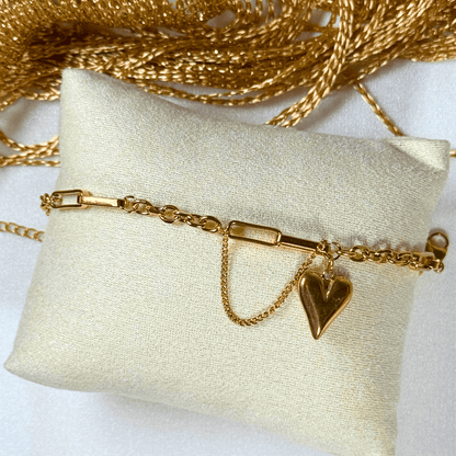 Gold bracelet with a heart charm on a white pillow