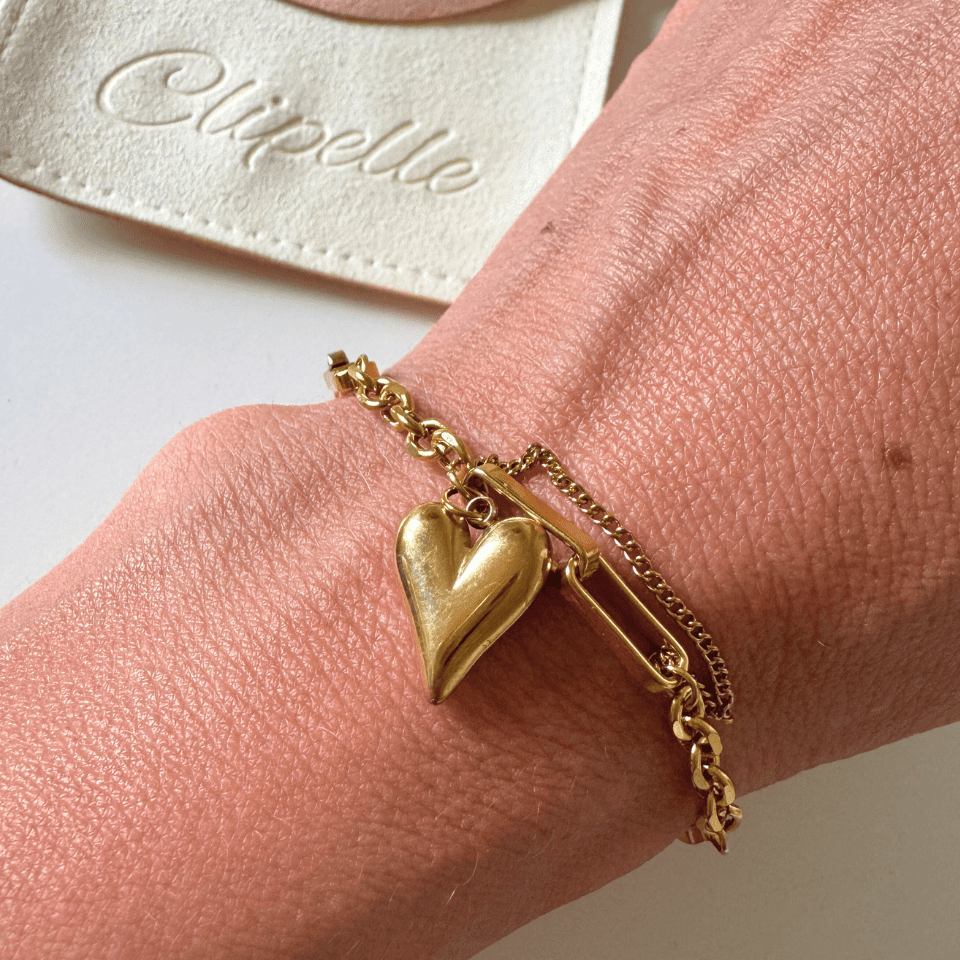 Gold heart-shaped bracelet on a wrist with a beige background