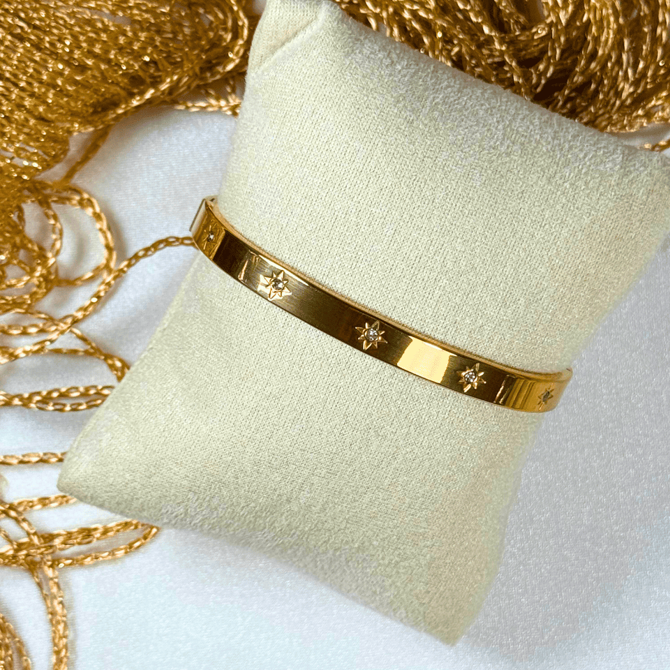 Gold bracelet on a beige cushion with gold chains in the background