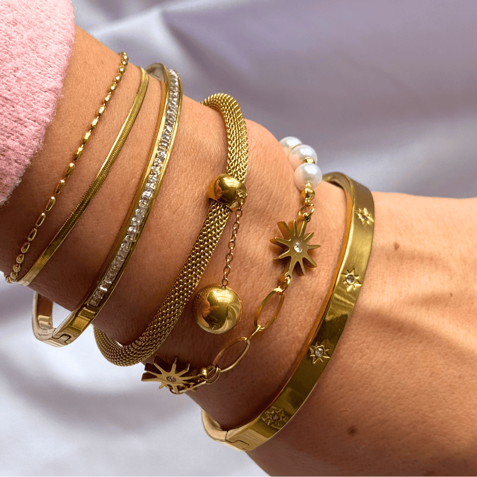 Close-up of a wrist wearing multiple gold bracelets on a light background