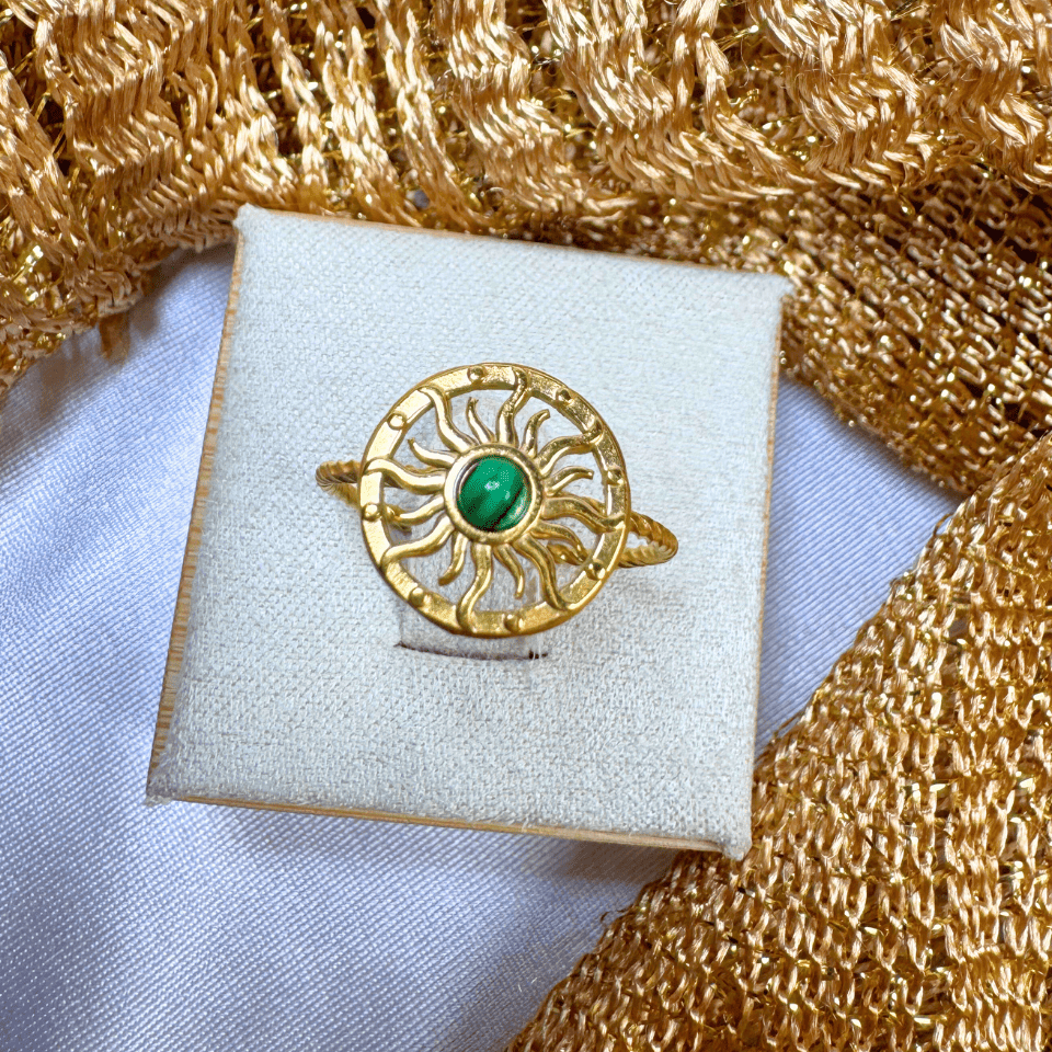 Gold ring with a green gemstone on a white cushion against a gold textured background