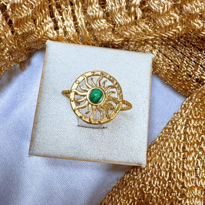 Gold ring with a green gemstone on a white cushion against a gold textured background