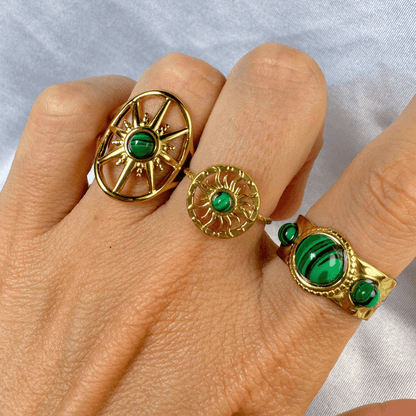 Gold rings with green gemstones on a hand against a light gray background