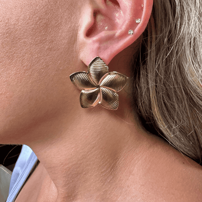 Gold floral earring worn by a person with blonde hair.