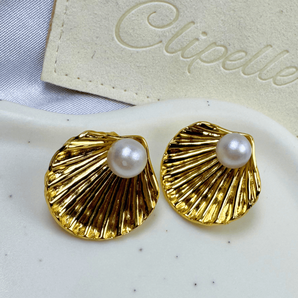 Gold shell-shaped earrings with pearl centers on a white surface, featuring the brand 'Clipette'.