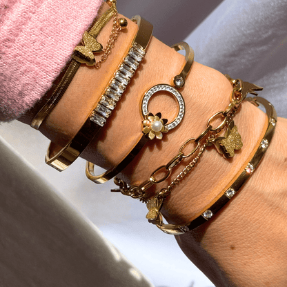 Multiple gold bracelets with various designs on a wrist against a neutral background