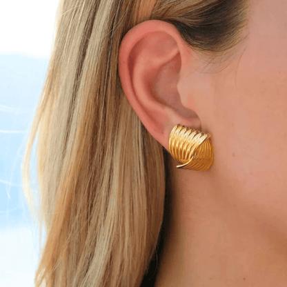 Gold earring worn by a person with blonde hair, against a blurred background