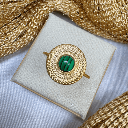 Gold brooch with green gemstone on a white cushion, surrounded by gold fabric.