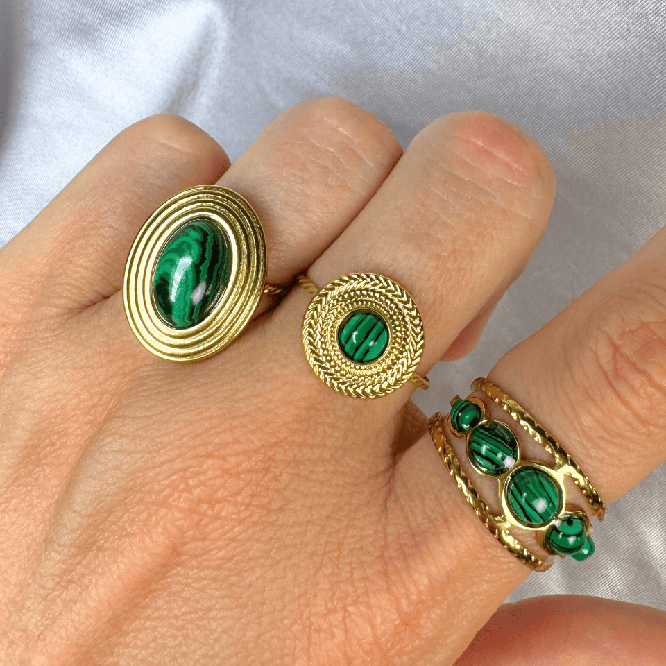 Gold rings with green gemstones on a hand against a light background