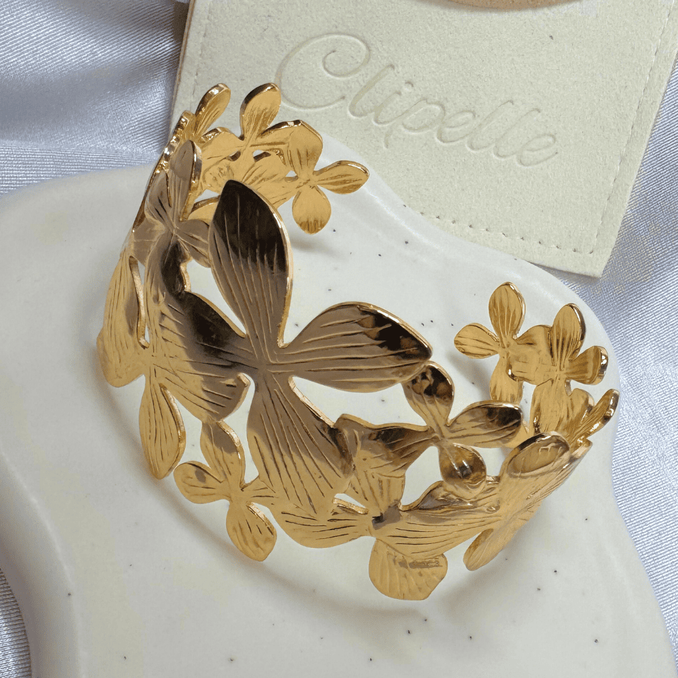 Gold floral bracelet on a white surface with 'Clipelle' branding in the background.