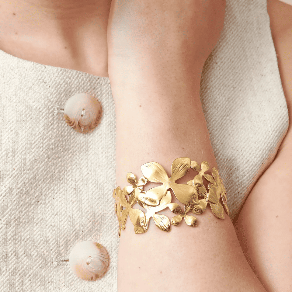 Gold bracelet on a wrist with seashells in the background