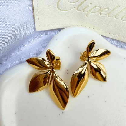 Gold leaf-shaped earrings on a white stone with 'Clipette' branding in the background.