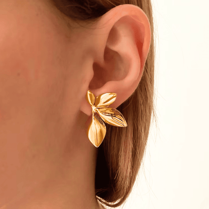 Gold leaf earring worn by a person on a white background