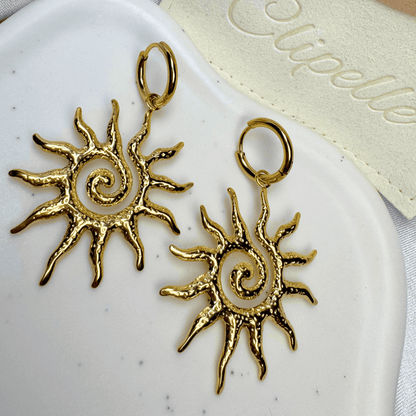 Gold sun-shaped earrings on a white dish with a beige cloth background