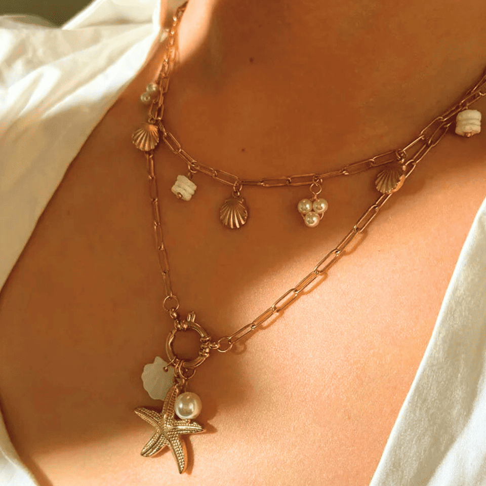 Close-up of a person wearing a gold necklace with starfish and shell charms.