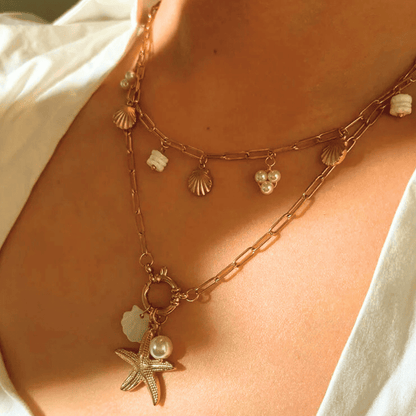 Close-up of a person wearing a gold necklace with starfish and shell charms.