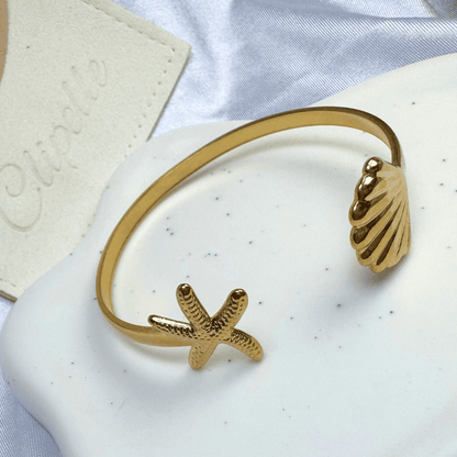 Gold bracelet with starfish and shell designs on a white surface