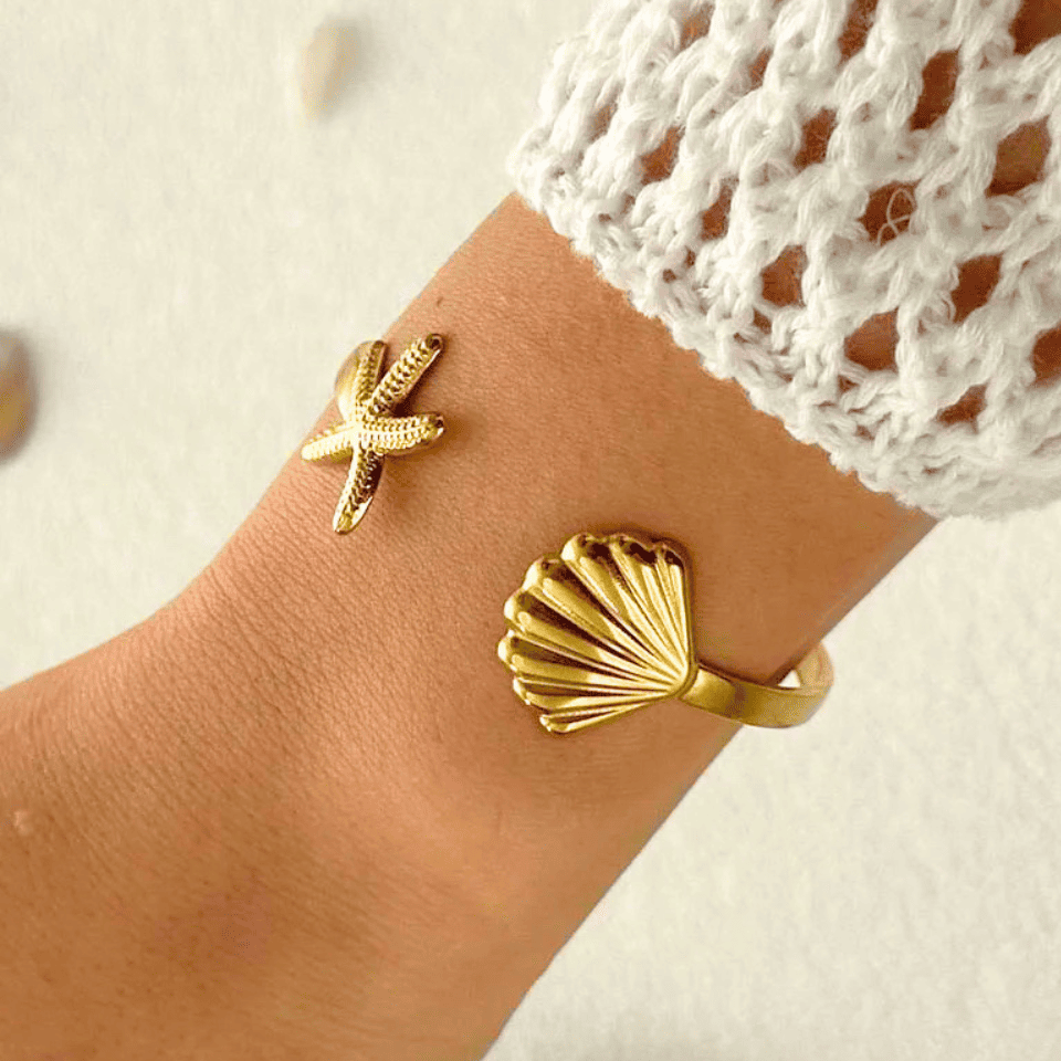 Gold starfish and shell bracelet on a wrist with a white textured background