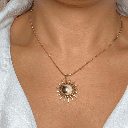 Gold sun-shaped pendant necklace on a person wearing a light-colored top.