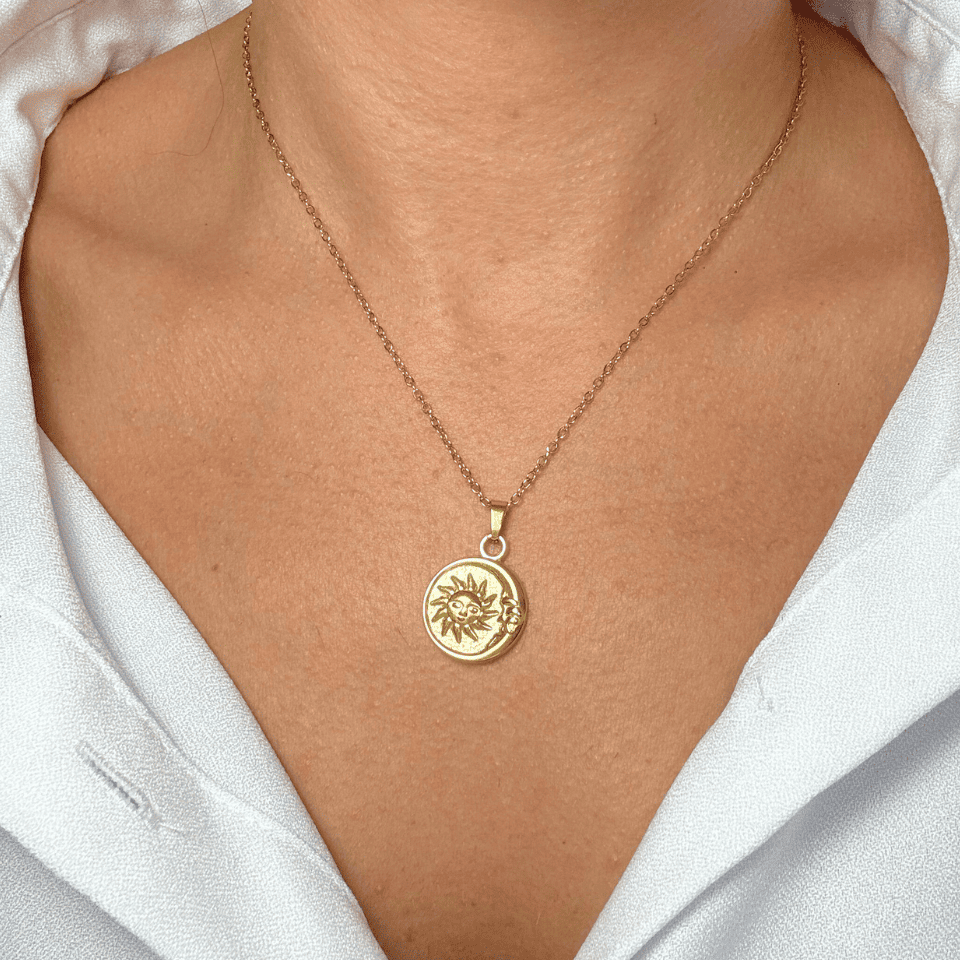 Gold necklace with a sun pendant worn by a person against a white background
