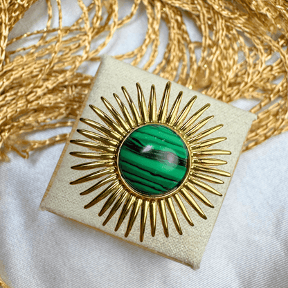 Gold brooch with green gemstone on a white and gold textured background