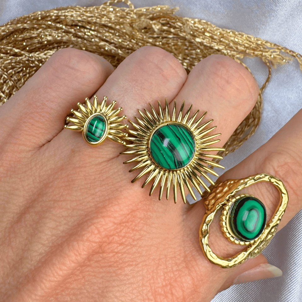 Gold rings with green gemstones on a hand, with gold thread in the background.
