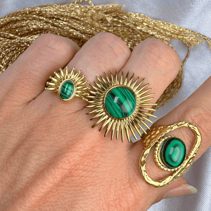 Gold rings with green gemstones on a hand, with gold thread in the background.