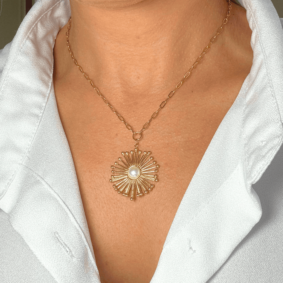 Gold necklace with a sunflower pendant worn by a person in a white shirt.