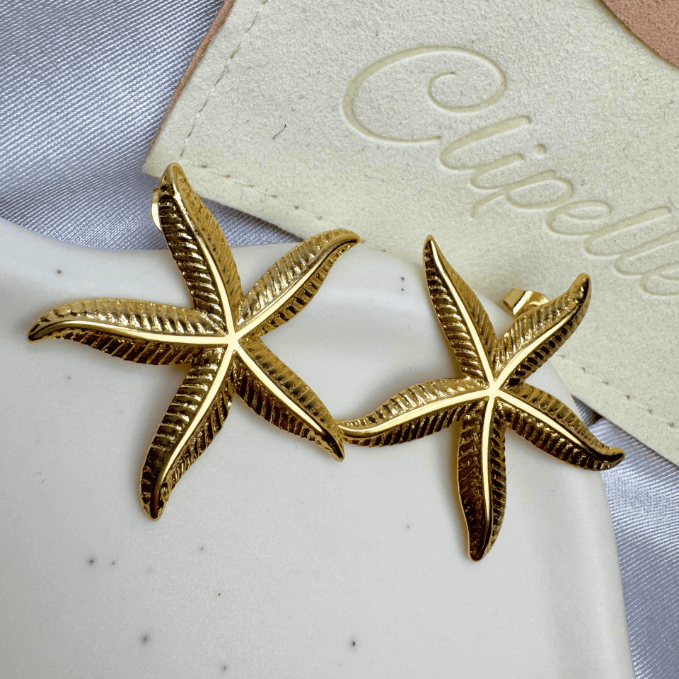 Gold starfish earrings on a white surface with a branded card in the background.