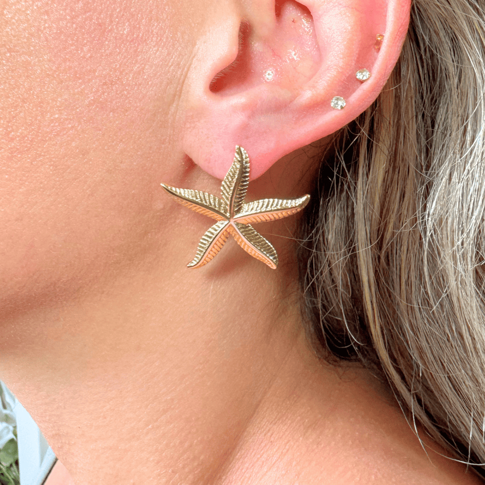 Close-up of a person wearing a gold starfish earring.