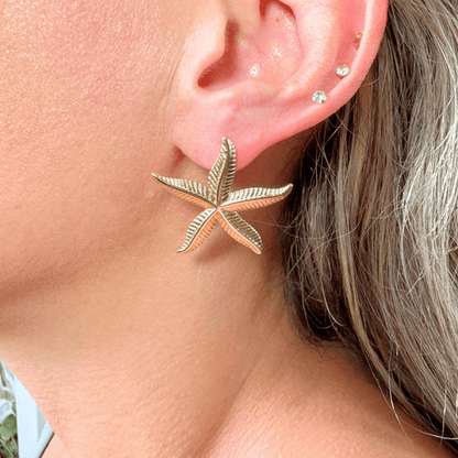 Close-up of a person wearing a gold starfish earring.