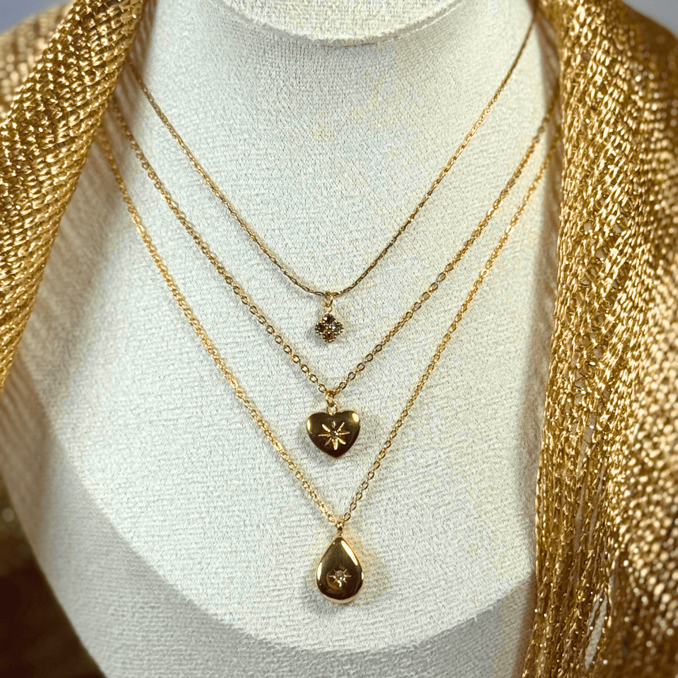 Three gold necklaces with heart and teardrop pendants on a mannequin bust.