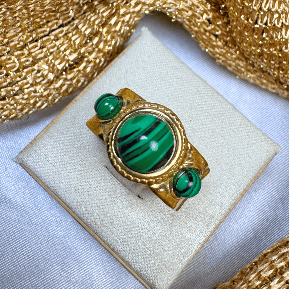 Gold ring with green gemstones on a white cushion, gold fabric background
