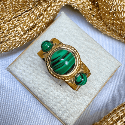 Gold ring with green gemstones on a white cushion, gold fabric background