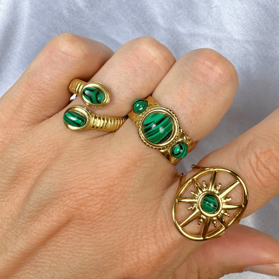 Gold rings with green gemstones on a hand against a light gray background